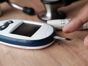 Ilustrasi glukometer dengan strip uji berdarah dan alat tusuk jari di meja kayu