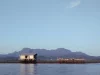 Ilustrasi rumah panggung dan keramba di atas laut dengan siluet Gunung Sepincan di Pulau Lingga, Kepulauan Riau