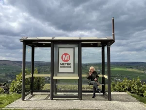 Ilustrasi seorang perempuan duduk menunggu di halte bus tepi perbukitan, Yorkshire, Inggris