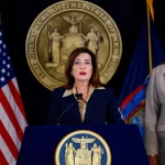 Gubernur New York Kathy Hochul berbicara di podium didampingi Letitia James