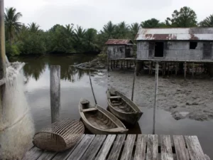Ilustrasi dua sampan kayu tertambat di dermaga papan dekat rumah panggung beratap seng