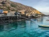 Ilustrasi rumah panggung kayu kampung nelayan di pulau berbukit kering dengan perahu bercadik