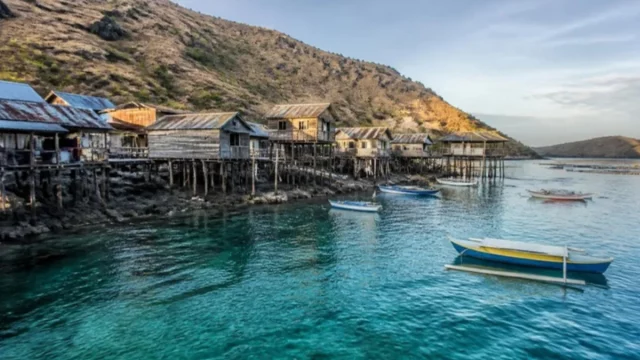 Ilustrasi rumah panggung kayu kampung nelayan di pulau berbukit kering dengan perahu bercadik