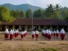 Ilustrasi murid SD berseragam merah putih berbaris di halaman sekolah desa berbukit