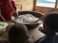 Ilustrasi papeda diaduk dengan tongkat kayu di mangkuk besar, anak-anak menonton dari belakang