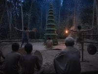 Ilustrasi menara anyaman daun di tengah hutan dengan dua penari serta penabuh rebana dan gong