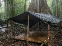 Ilustrasi pondok kayu beratap terpal berlantai anyaman di hutan hujan dekat sungai kecil