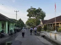 Ilustrasi jalan kota kabupaten pada pagi hari dengan puskesmas, sekolah, dan siswa berjalan