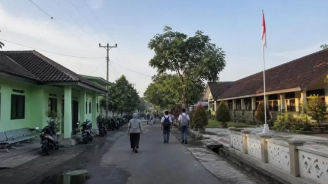 Ilustrasi jalan kota kabupaten pada pagi hari dengan puskesmas, sekolah, dan siswa berjalan