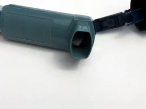Ilustrasi inhaler asma berwarna hijau kebiruan dengan tutup terbuka di atas latar putih