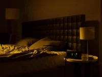 Ilustrasi kamar tidur remang dengan ranjang kusut dan jam digital menyala di nakas