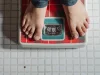 Ilustrasi sepasang kaki anak berdiri di timbangan badan di lantai keramik putih