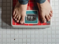 Ilustrasi sepasang kaki anak berdiri di timbangan badan di lantai keramik putih
