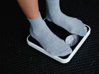 Ilustrasi sepasang kaki berkaus abu-abu berdiri di atas timbangan badan putih