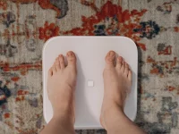 Ilustrasi sepasang kaki telanjang berdiri di atas timbangan pintar putih di karpet