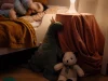 Ilustrasi sudut kamar tidur anak bercahaya redup dengan boneka dan lampu meja