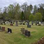 Deretan batu nisan di halaman makam Gereja Hallaryd, Swedia, dengan bangunan gereja putih