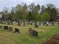 Deretan batu nisan di halaman makam Gereja Hallaryd, Swedia, dengan bangunan gereja putih