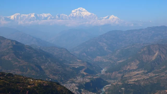 Ilustrasi Kota Baglung Bazar di lembah perbukitan dengan puncak bersalju Dhaulagiri di kejauhan, Nepal