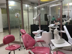 Ilustrasi kursi periksa gigi merah marun dan unit dental di ruang klinik berdinding kaca