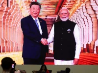 Layar besar menampilkan Narendra Modi berjabat tangan dengan Xi Jinping