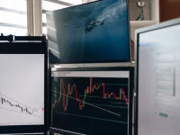 Beberapa layar pemantau menampilkan grafik lilin pergerakan harga saham di meja kerja