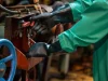 Ilustrasi lengan pekerja bersarung tangan karet hitam mengoperasikan tuas mesin industri