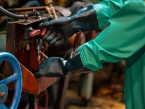 Ilustrasi lengan pekerja bersarung tangan karet hitam mengoperasikan tuas mesin industri
