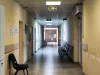 Ilustrasi lorong rumah sakit yang sepi dengan deretan kursi tunggu hitam dan pintu terbuka