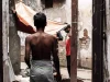 Seorang lelaki bersarung berjalan di lorong sempit berdinding kusam di Dhaka, Bangladesh