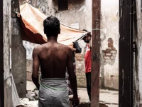 Seorang lelaki bersarung berjalan di lorong sempit berdinding kusam di Dhaka, Bangladesh