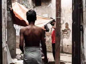 Seorang lelaki bersarung berjalan di lorong sempit berdinding kusam di Dhaka, Bangladesh