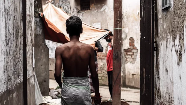 Seorang lelaki bersarung berjalan di lorong sempit berdinding kusam di Dhaka, Bangladesh