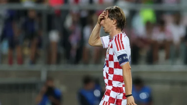 Luka Modric memegang kepala saat berjalan di lapangan dengan seragam kotak-kotak merah putih Kroasia