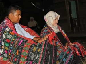 Ilustrasi pasangan berselimut ulos menari tortor pada malam hari dalam adat perkawinan Batak Toba