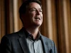 Mantan Direktur FBI James Comey berjas kotak-kotak tersenyum di belakang panggung