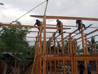 Ilustrasi warga bergotong royong mendirikan rangka kayu rumah panggung dalam tradisi mappatettong bola Bugis-Makassar