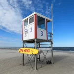 Ilustrasi menara jaga penyelamat DLRG dengan papan selamat kuning di pantai berpasir Juist, Jerman