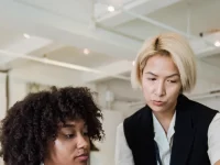 Seorang mentor perempuan memperhatikan rekan muda yang bekerja di ruang kantor