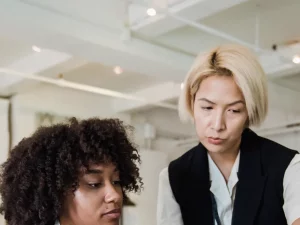 Seorang mentor perempuan memperhatikan rekan muda yang bekerja di ruang kantor