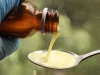 Ilustrasi tangan bersarung karet biru menuang obat cair dari botol ke sendok