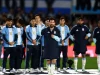 Lionel Messi berjaket timnas Argentina mengangkat tangan di lapangan dikelilingi rekan setim