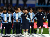 Lionel Messi berjaket timnas Argentina mengangkat tangan di lapangan dikelilingi rekan setim