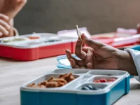 Ilustrasi tangan murid di meja dengan kotak bekal bersekat berisi makanan