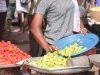 Pedagang perempuan menuang sayur hijau ke nampan di samping tumpukan cabai, pasar di Ghana