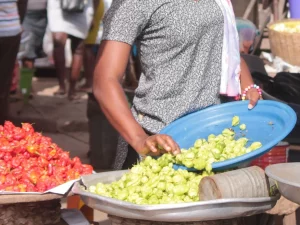 Pedagang perempuan menuang sayur hijau ke nampan di samping tumpukan cabai, pasar di Ghana