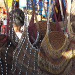 Ilustrasi deretan noken rajutan serat berwarna alami tergantung di lapak penjual, Papua