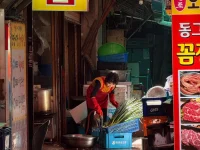 Ilustrasi pedagang bermasker menyiapkan daun bawang di kios pasar berpapan nama aksara Korea, Korea Selatan