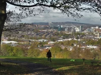 Ilustrasi seorang pejalan kaki di lereng berumput Taman Meersbrook dengan panorama kota Sheffield, Inggris