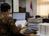 Ilustrasi pemeriksa pajak berkemeja batik meneliti tumpukan dokumen ekspor pulp di meja kerja